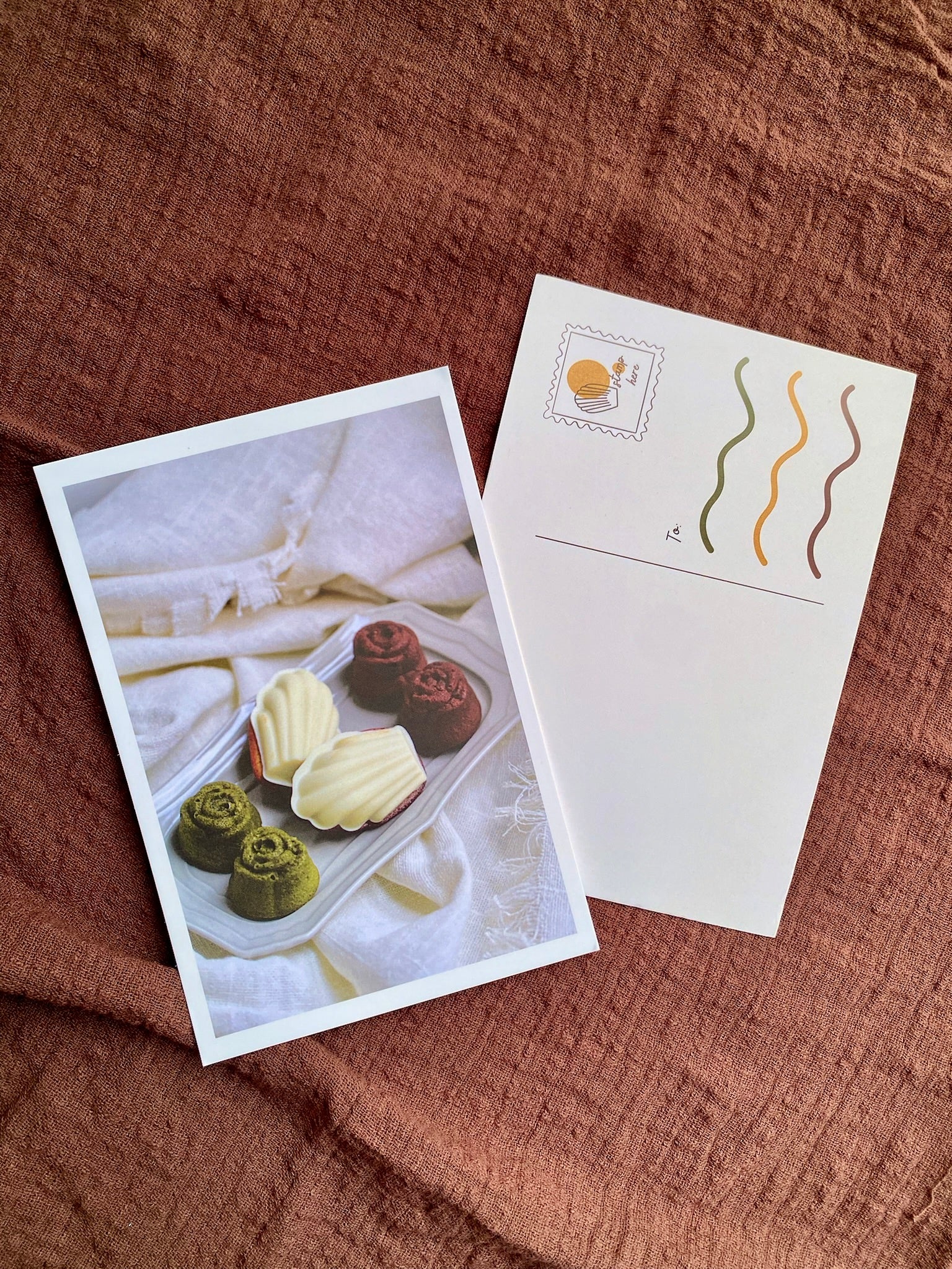 Two postcards on a textured brown surface, one with a dessert image and the other with wavy line design.