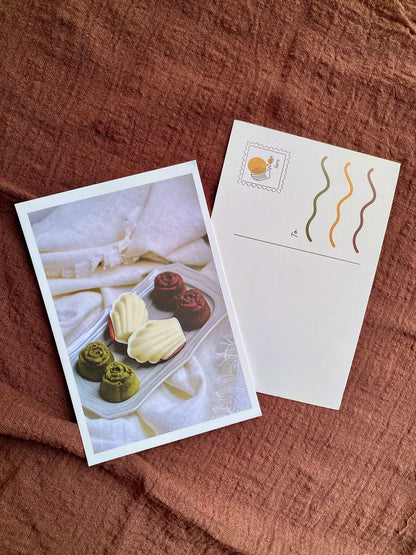 Two postcards on a textured brown surface, one with a dessert image and the other with wavy line design.