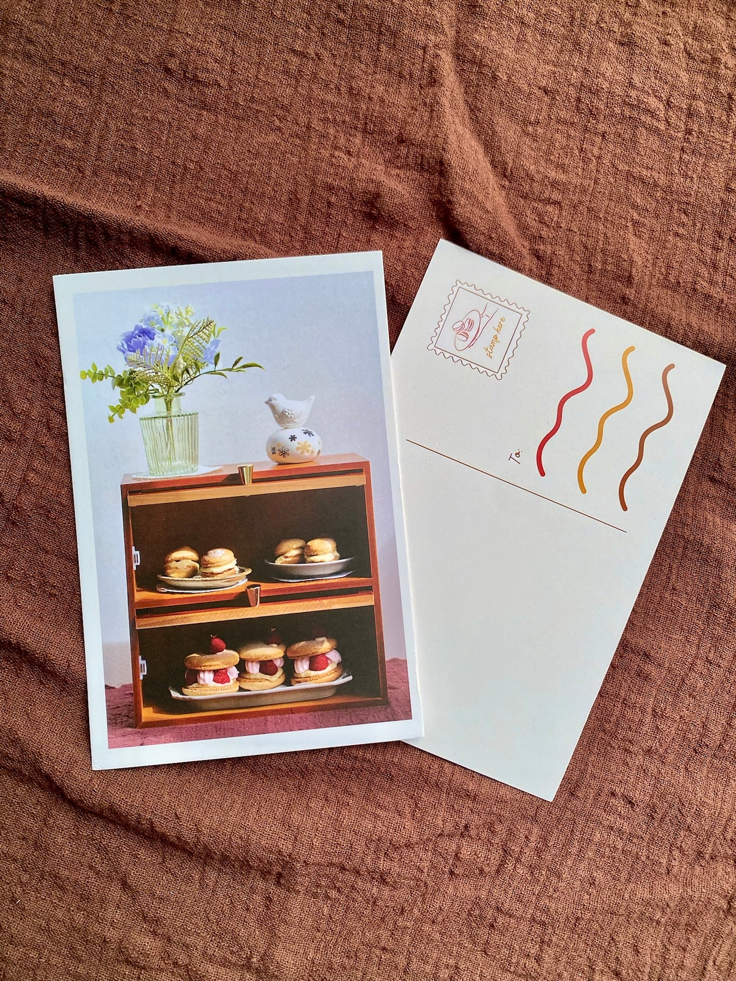 Greeting card with a cabinet of sweets illustration and matching envelope on a brown fabric background