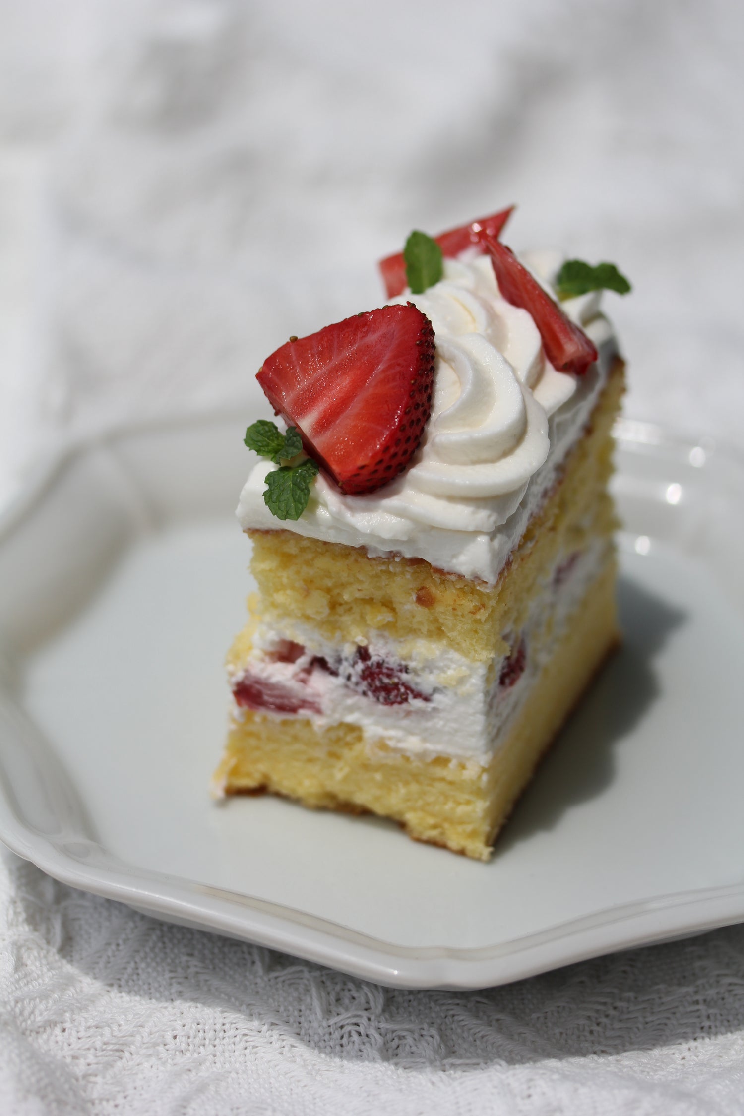 Slice of layered cake with strawberries and cream on a white plate.